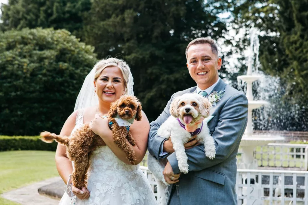 Bride and groom each holding their dogs beside the fountain at Hawkesyard Estate.