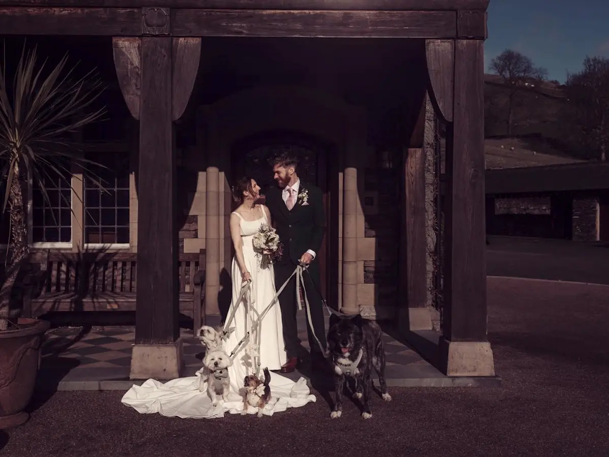 Bride and groom with three dogs on leads outside a dog-friendly wedding venue