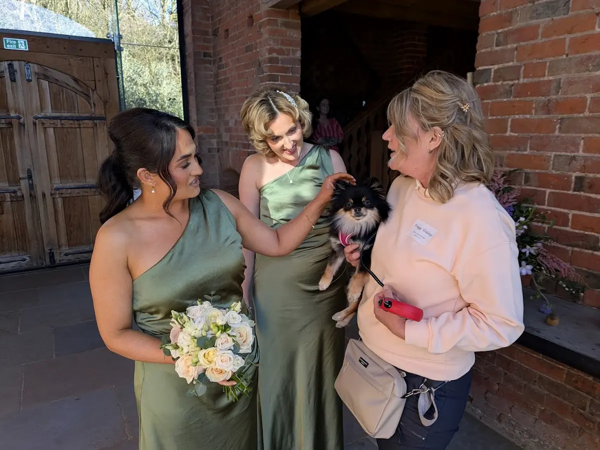 Waggy Wedding Events dog chaperone holding a small Pomeranian with bridesmaids at a wedding venue
