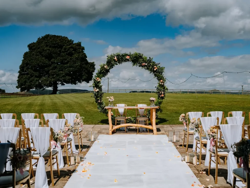 Outdoor wedding ceremony setup at Heaton House Farm with a circular floral arch and white aisle runner overlooking the Cheshire countryside.